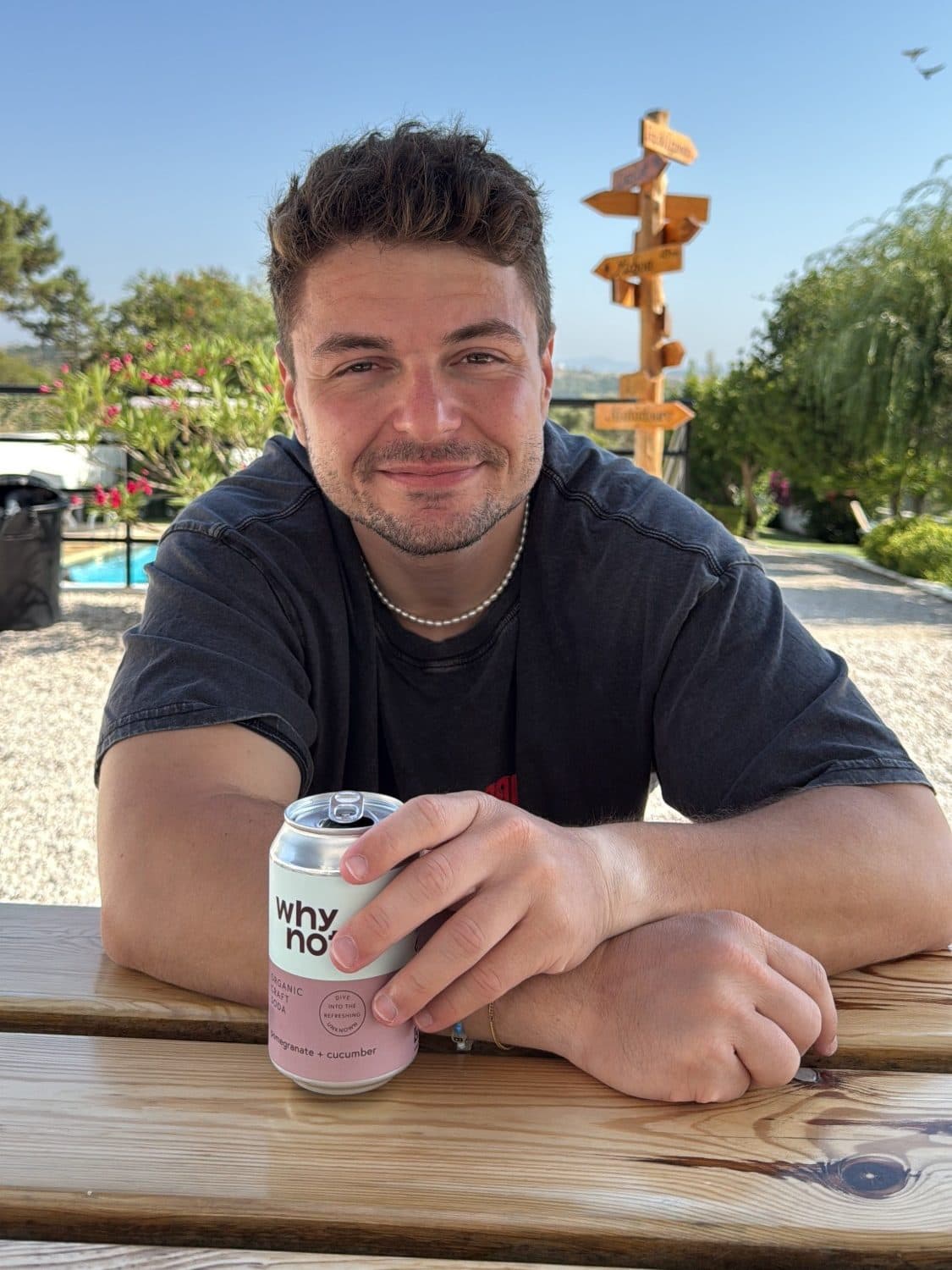 Florian Raschle at a wooden table with a can of craft soda, a signpost and blue sky behind him